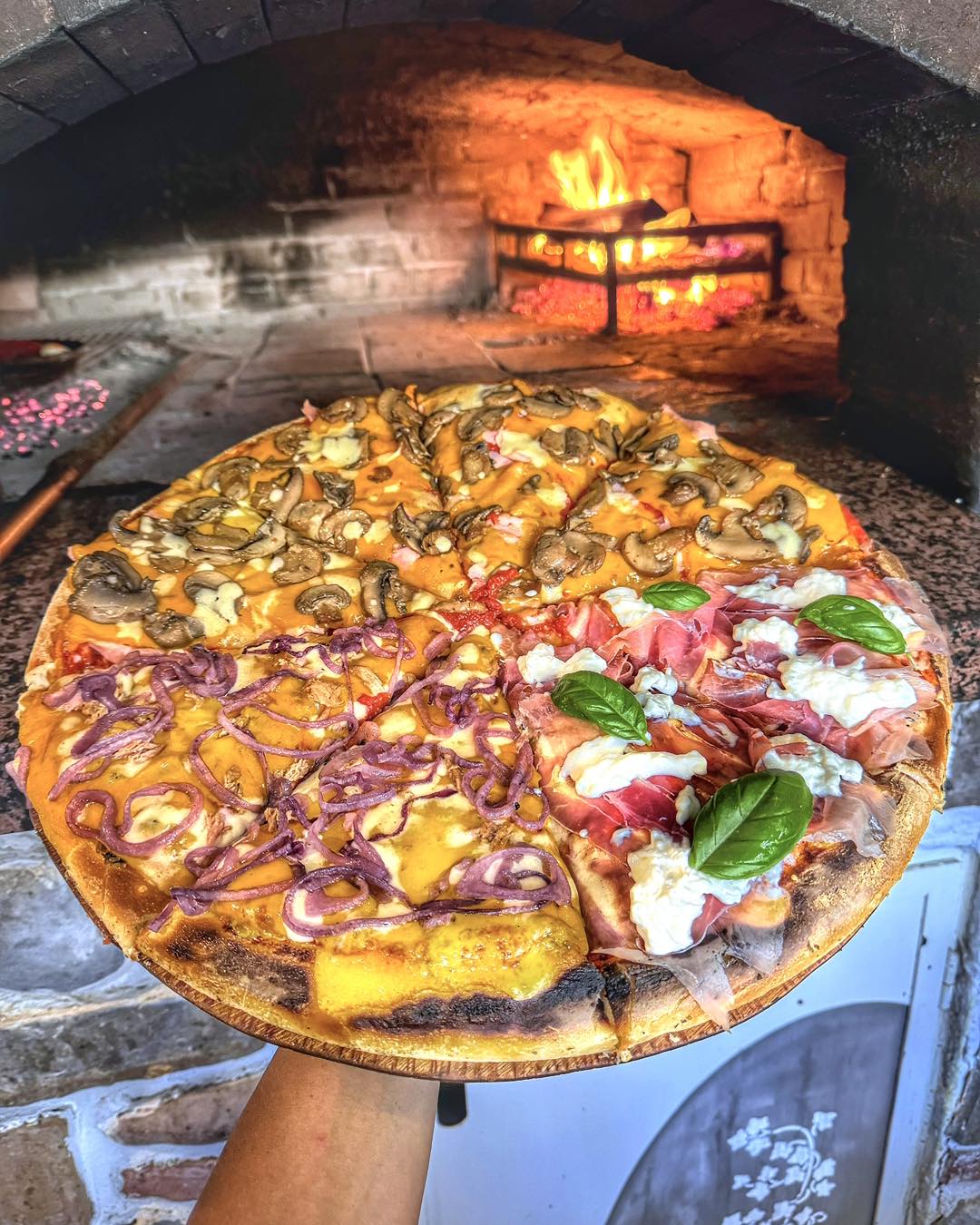 Pizza intera a quattro gusti davanti al forno a legna acceso